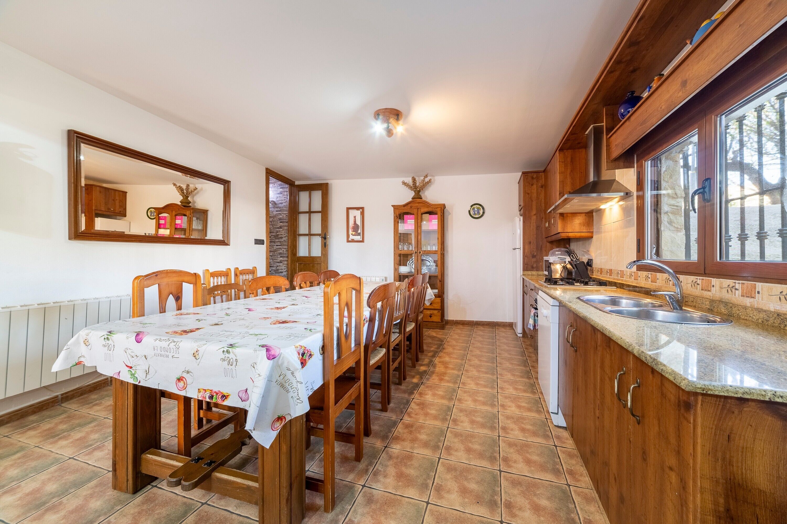 Comedor con una mesa dispuesta para cuatro personas, sillas de madera, cocina con encimeras de granito y una ventana.