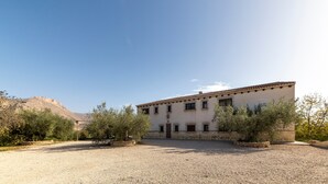 A building with a tiled roof, a gravel driveway, and surrounding vegetation.