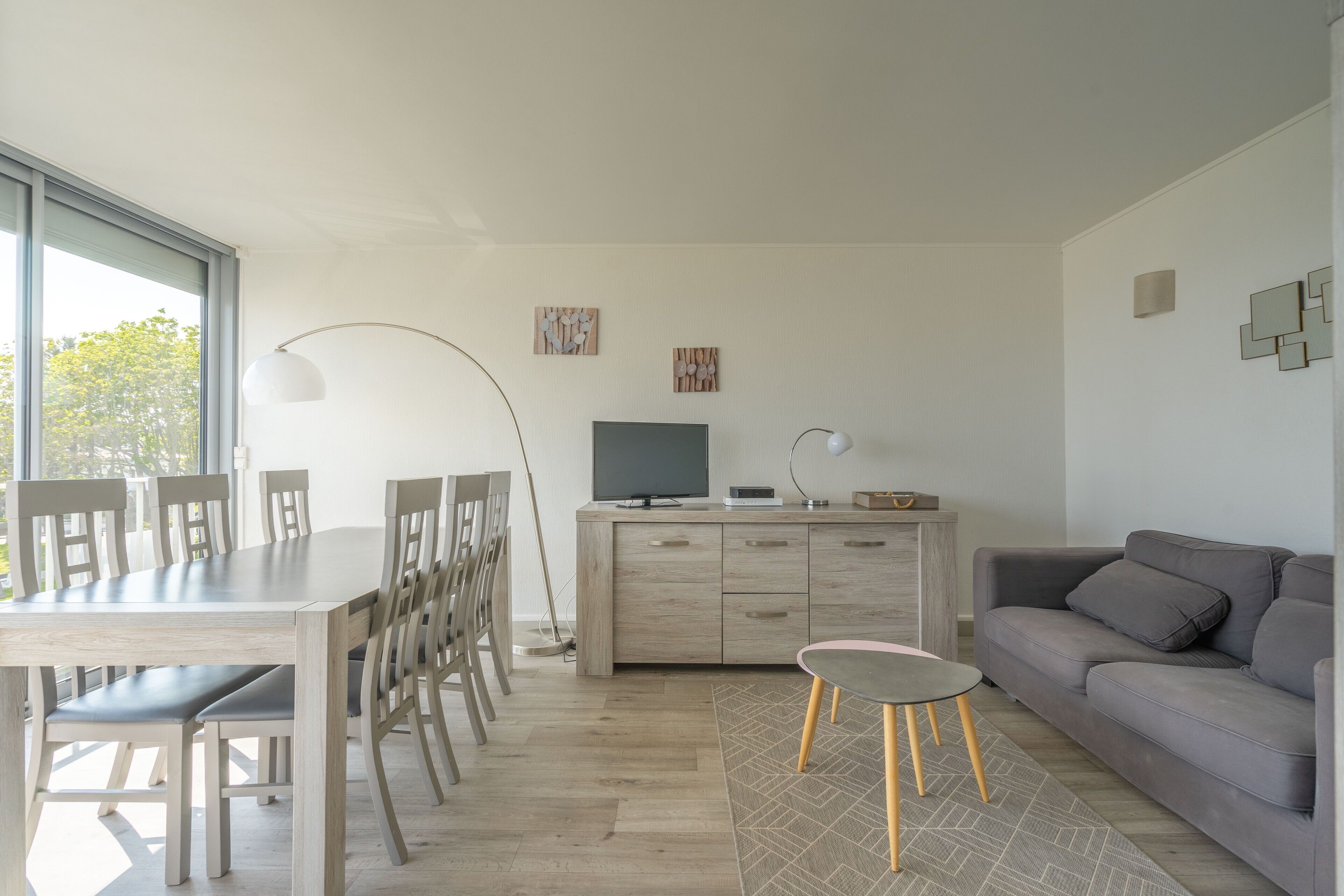 A modern living room with a dining table, chairs, a sofa, a TV, and artwork on the walls.