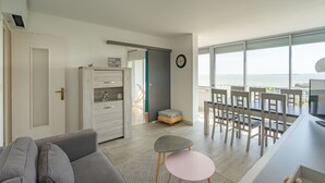 A modern living room with a sofa, a small table, a dining area with chairs, a television, and a view of the sea. - Holiday Apartment "Mer Beau Rivage" near Beach with Private Terrace & Wi-Fi (ROYAN)