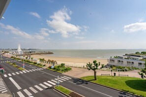 A coastal road with a beach, a Ferris wheel, and a modern building with a flat roof.