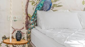 Un lit avec une literie blanche, un fauteuil suspendu en macramé et un paon décoratif.