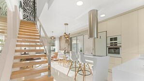 Een moderne keuken met een centraal eiland, een trap met houten treden en een eethoek met witte stoelen.