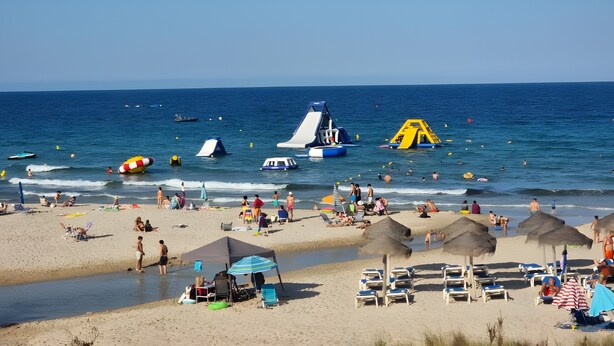 Een strand met ligbedden, parasols en een heldere lucht.
