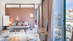 A modern living room with a sofa, a dining table, and a view of the city through large windows. - City and the Sea by Wonderful Italy (Genoa)