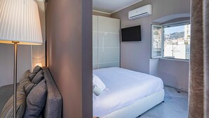 A modern bedroom with a bed, a TV, an air conditioning unit, and a window with a city view. - City and the Sea by Wonderful Italy (Genoa)
