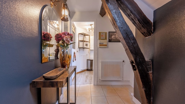 Een hal met een houten console tafel, een spiegel en een bloemenvaas. Er is een trap met zichtbare houten balken en een witte radiator aan de muur.