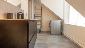 Een compacte keuken met een ingebouwde koelkast, een wasmachine en een houten ladder tegen de muur.