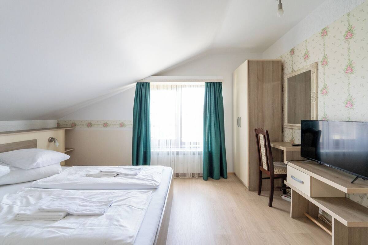 Una habitación de hotel con cama, escritorio con televisor y ventana con cortinas.