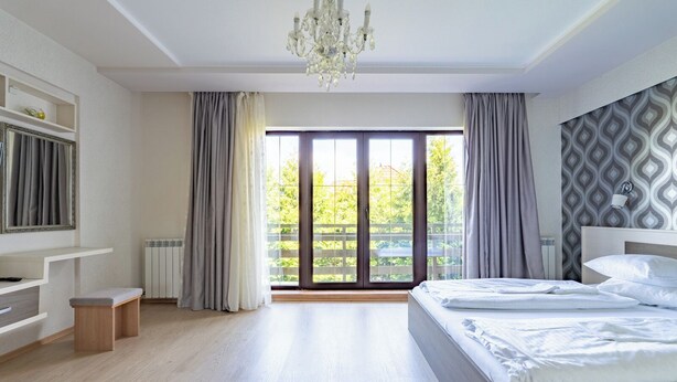Ein modernes Schlafzimmer mit einem großen Bett, einem Kronleuchter und Blick auf Grün durch das Fenster.