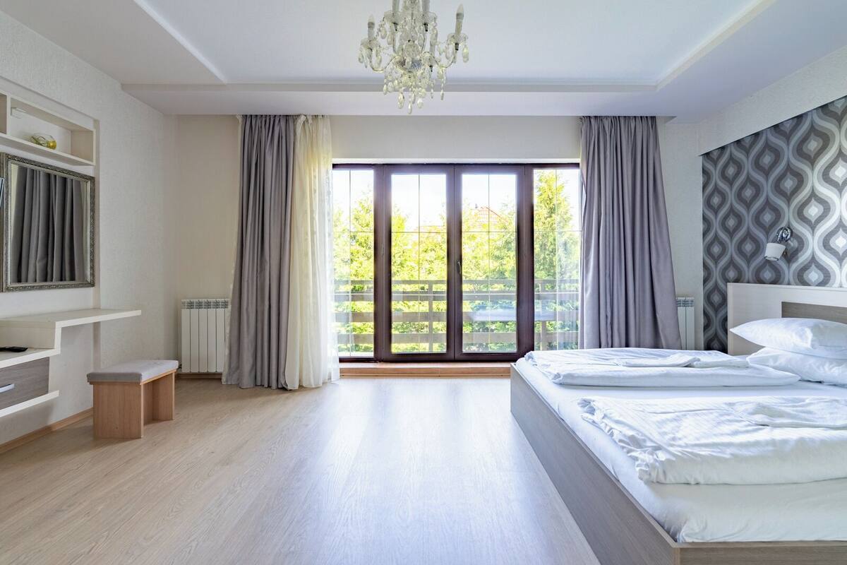 Un dormitorio moderno con una cama grande, una araña y vistas al verdor por la ventana.