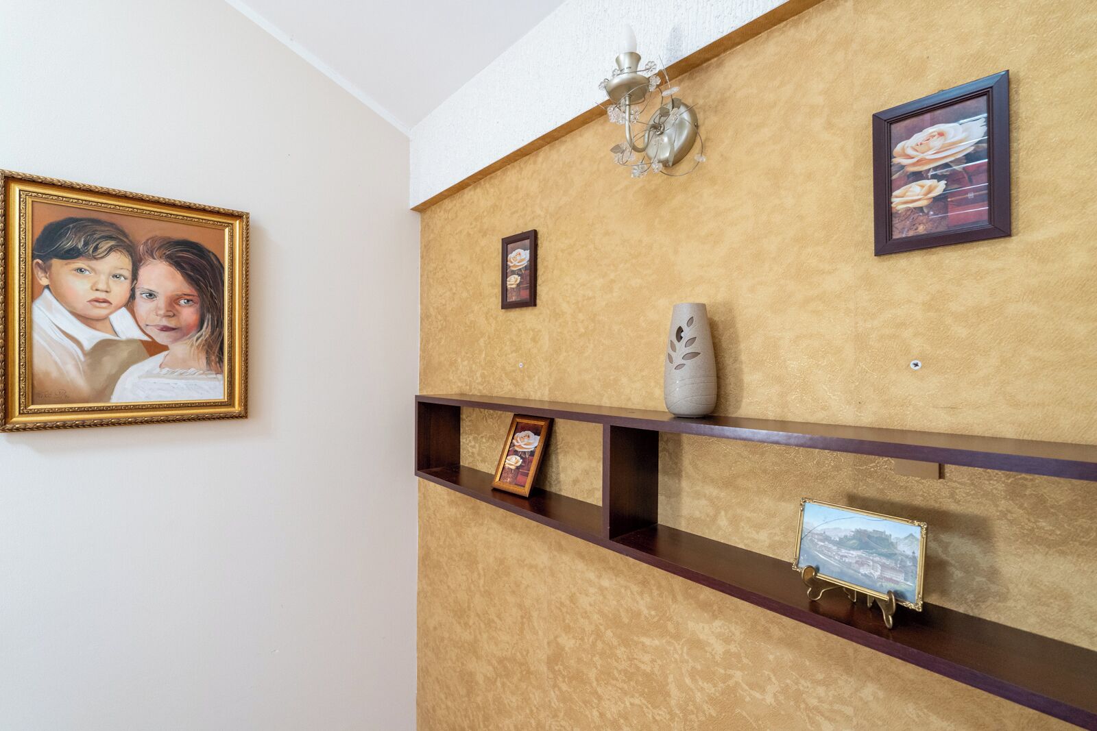 Un mur orné d’un portrait encadré, d’un vase et d’un tableau représentant un paysage.