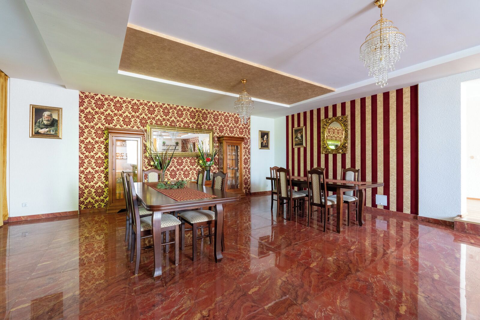 A spacious dining area with a polished marble floor, a large dining table surrounded by chairs, and a chandelier.