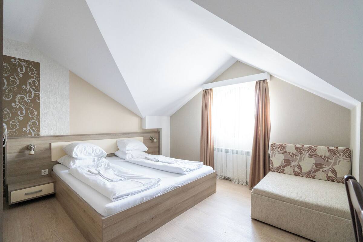 Un dormitorio con una cama de madera, una mesita de noche, una silla y una ventana con cortinas.
