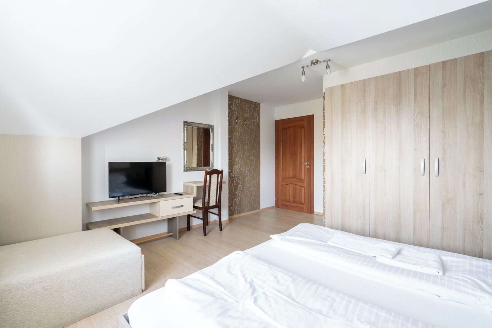 A bedroom with a bed, a desk with a TV, a chair, and a wardrobe.