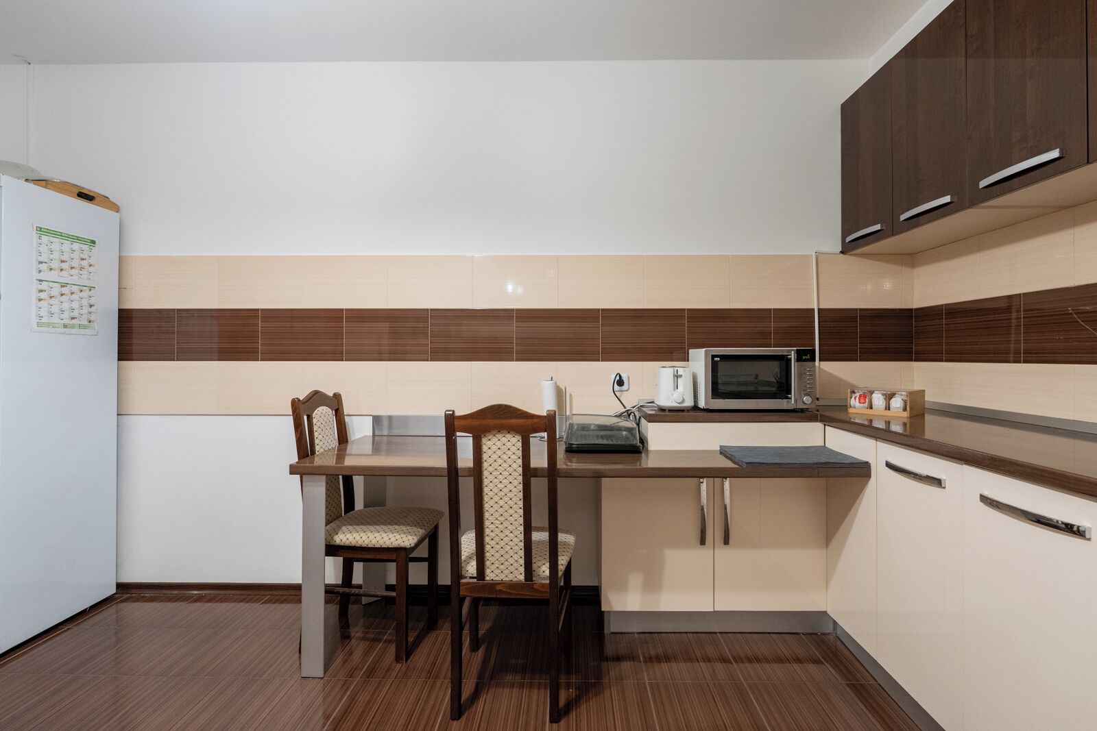 A compact kitchen with a wooden dining table, two chairs, a microwave, and cabinets.