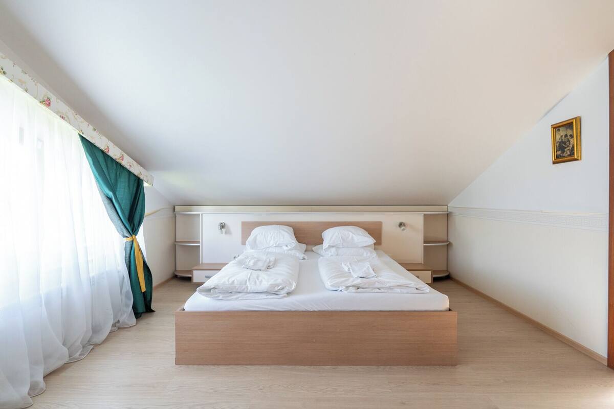 Un dormitorio con cama, mesita de noche, armario y ventana con cortinas.