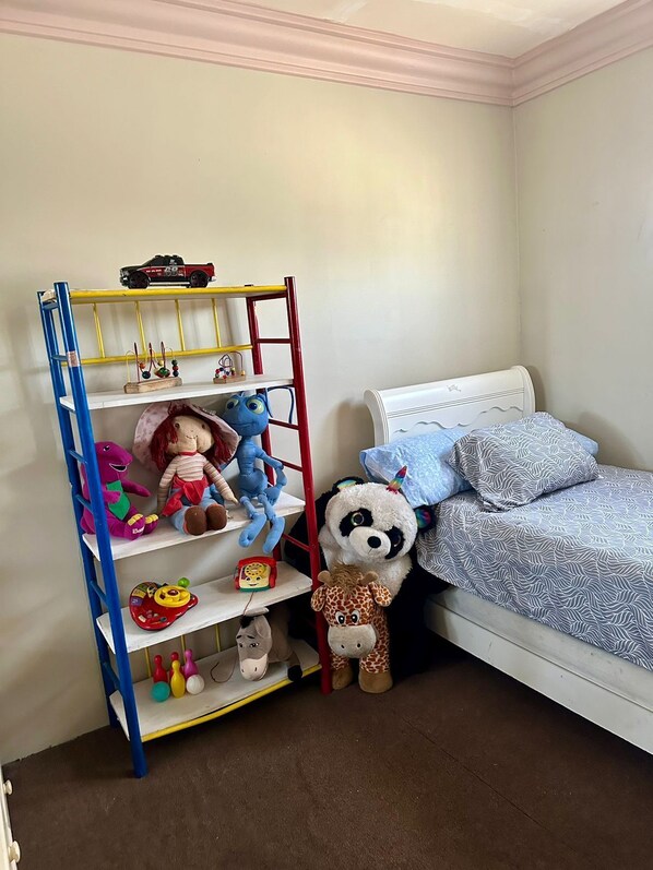 A child's bedroom with a bed, a toy shelf, and various stuffed toys.