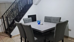 Een eetgedeelte met een tafel, stoelen, een trap en een airconditioning.