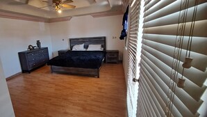 Een slaapkamer met een bed, een dressoir, een nachtkastje en een plafondventilator.