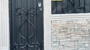 Een zwart metalen hekwerk met decoratieve versieringen, een brievenbus en een stenen muur.