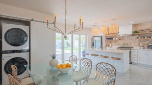 Una cocina moderna con una isla central, armarios blancos y un comedor con sillas de mimbre y una mesa de vidrio.
