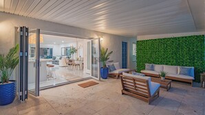 Un interior moderno con un acceso por puerta de vidrio que conduce a un comedor, una pared verde y un área de estar con sofá y mesa de centro.