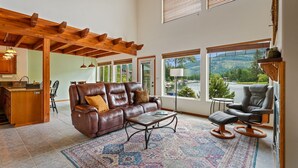 A spacious living room with a leather sofa, a coffee table, and a view of a mountainous landscape through large windows.