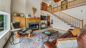 A spacious living room with a fireplace, leather sofa, and a staircase leading to an upper level.