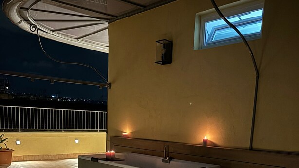 Un baño exterior moderno con bañera, una mesita con velas y una ventana.