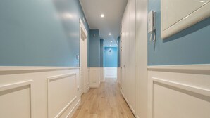 Un pasillo con suelo de madera y paneles blancos, que conduce a un baño con ducha e inodoro.