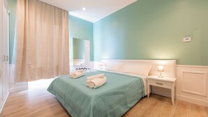 Un dormitorio con colcha verde, dos mesitas de noche con lámparas, un espejo grande y suelo de madera.