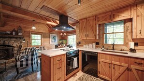 Una cocina de estilo rústico tipo cabaña, con armarios de madera, una chimenea de piedra y una silla a cuadros.