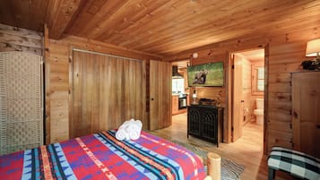 A wooden cabin room with a bed, a television, a desk, and a bathroom visible through an open door.