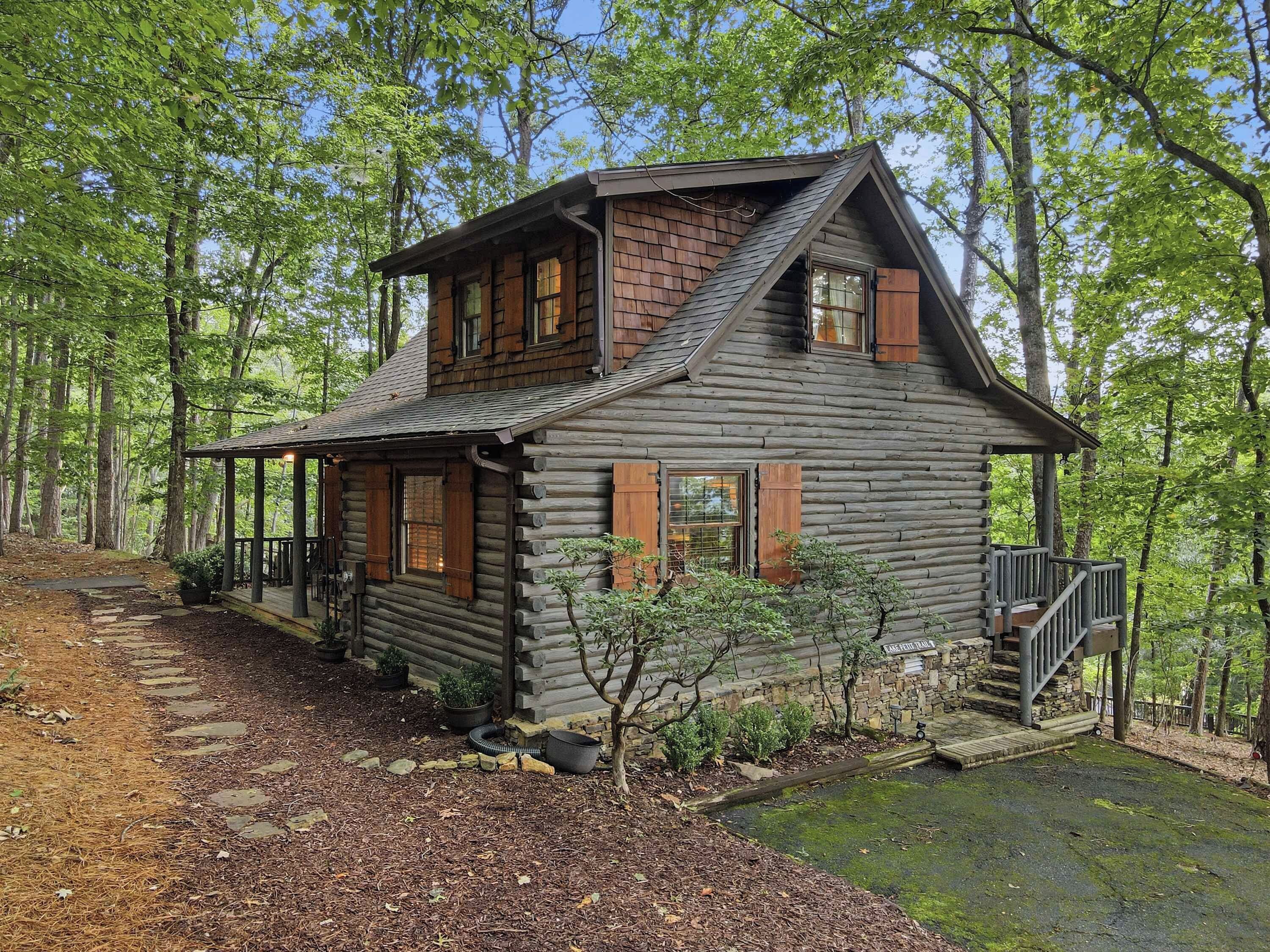 A log cabin with a porch, a stone staircase, and a small garden area.
