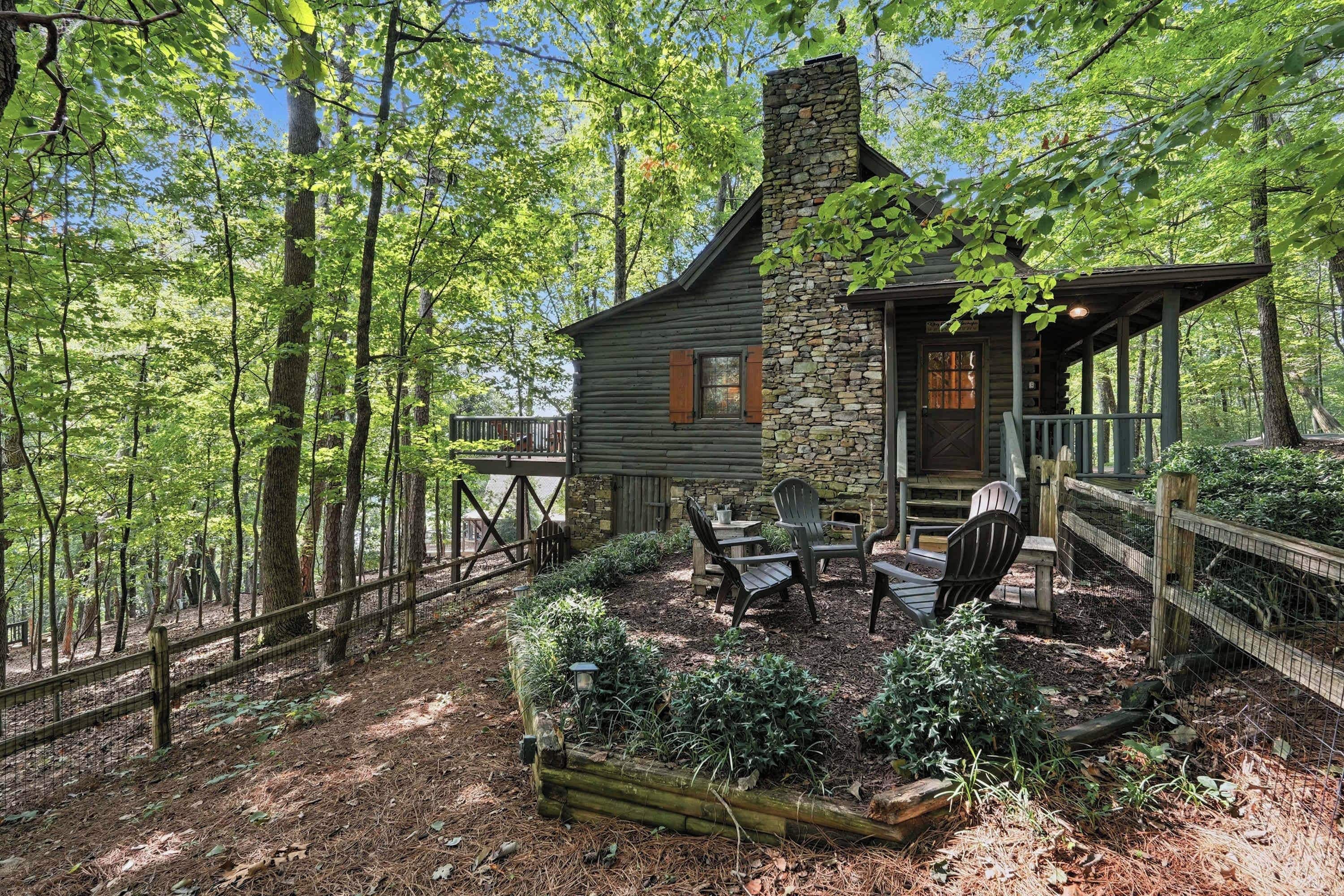 A cabin with a stone chimney, wooden deck, and outdoor seating area surrounded by trees.