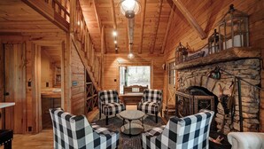L’intérieur d’un chalet accueillant, avec une cheminée en pierre, des fauteuils à carreaux disposés autour d’une table centrale et des murs en bois.