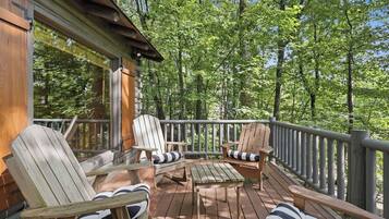 A wooden deck with Adirondack chairs and a table, surrounded by a forest.