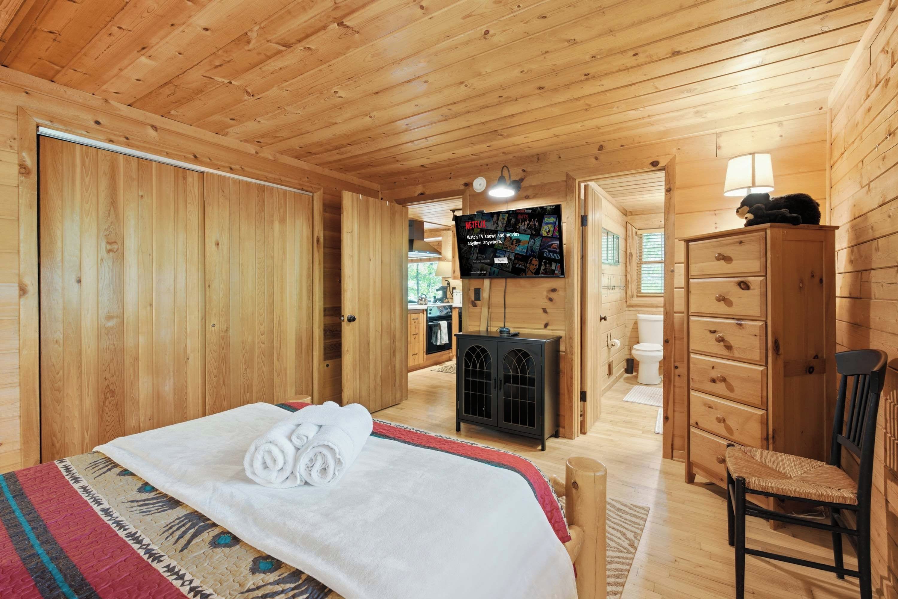 A wooden cabin interior with a bed, a television, a dresser, and a chair.