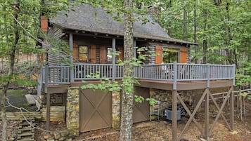 A cabin with a wooden deck, stone walls, and a pond.