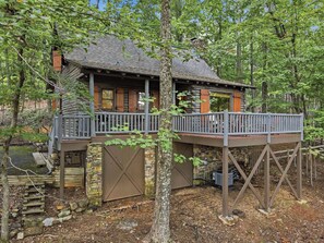 Une cabane dotée d’une terrasse en bois, de murs en pierre et d’un étang.