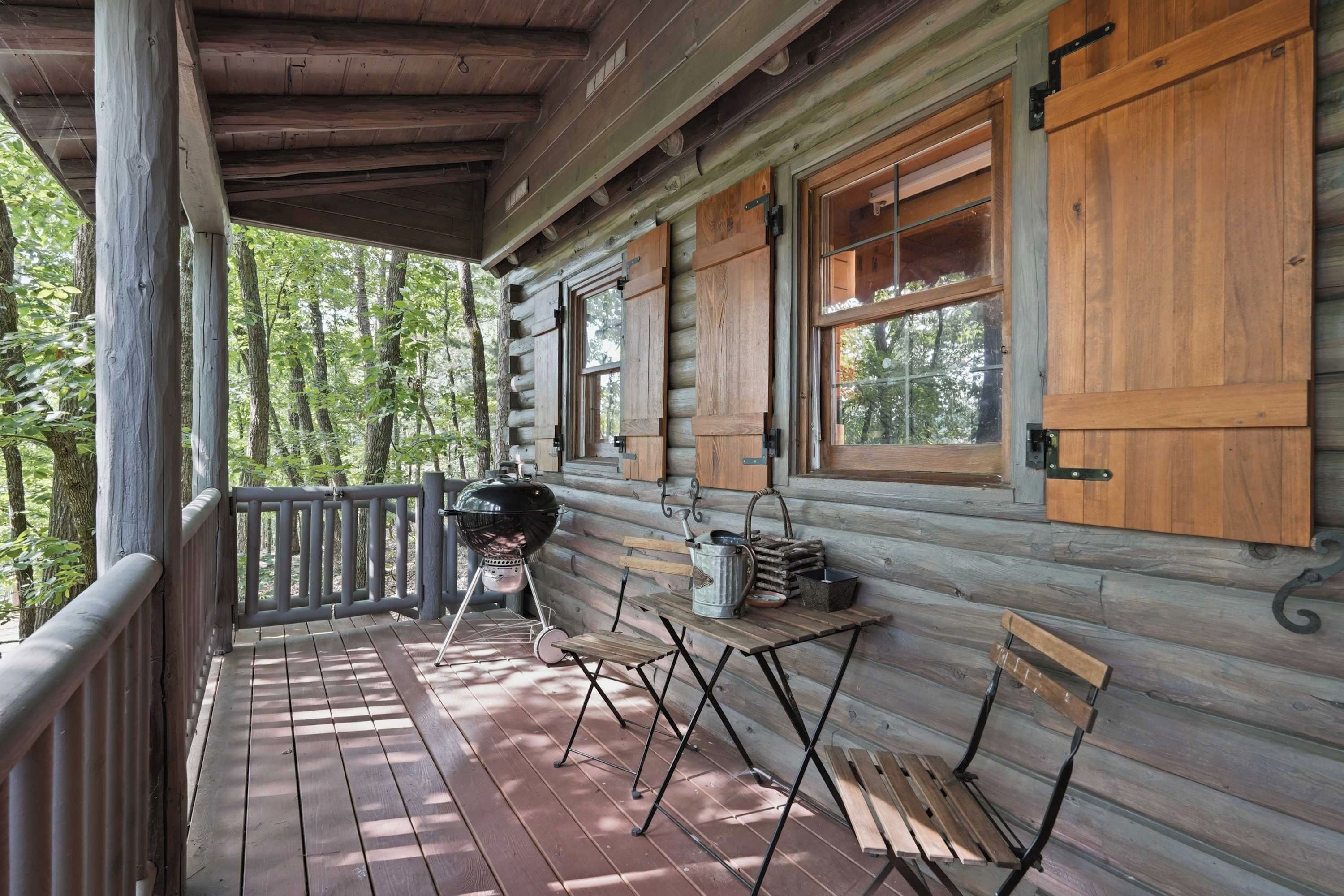 A wooden cabin with a porch, a grill, and a table with outdoor seating.