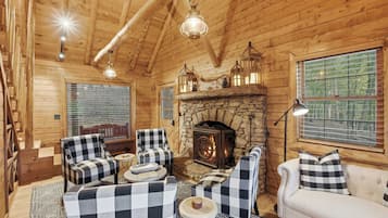 A cozy log cabin interior with a stone fireplace, checkered furniture, and large windows.