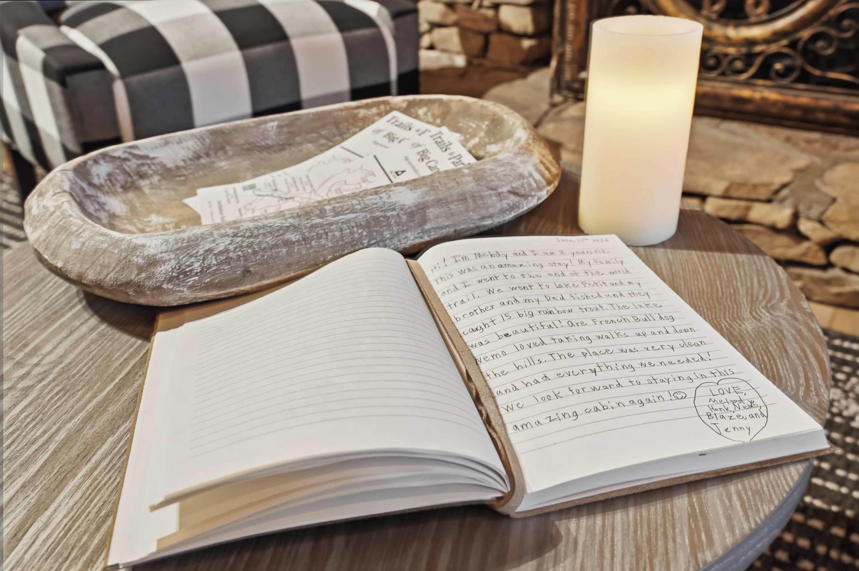 A notebook with handwritten text, a candle, and a tray with papers on a wooden table.