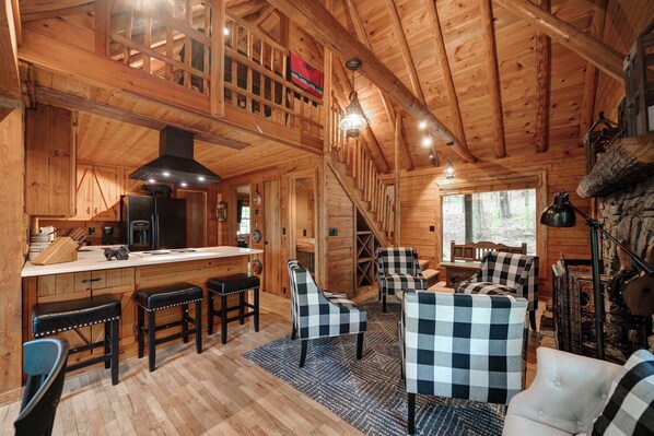 A wooden cabin interior with a kitchen, dining area, and seating. - The Guest House Historic Cabin in Big Canoe (Jasper)