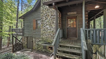 A rustic cabin with a stone wall, wooden steps, and a porch.