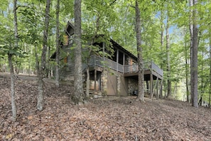 A log cabin with a stone foundation, surrounded by a forest. - The Guest House Historic Cabin in Big Canoe (Jasper)