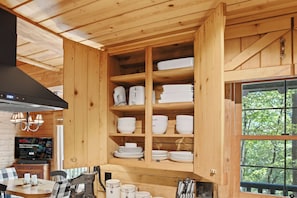 A wooden interior with a built-in kitchen area featuring shelves with bowls and plates, a dining table with chairs, and a television displaying a Netflix advertisement. - The Guest House Historic Cabin in Big Canoe (Jasper)