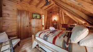 Un dormitorio de cabaña de madera acogedor, con cama, banco, televisor y escalera.