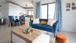 Een moderne woonkamer met een blauwe bank, een houten salontafel, en een eethoek met blauwe stoelen.